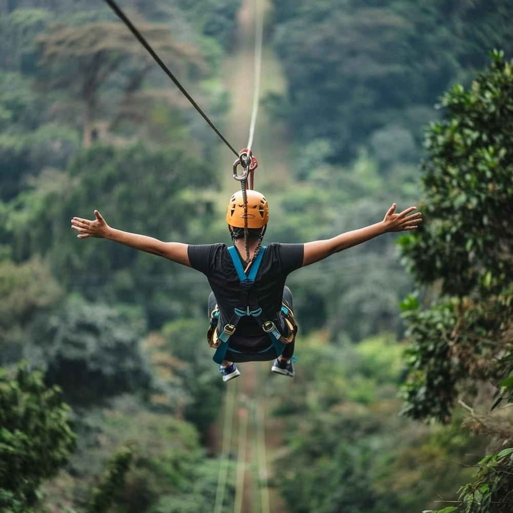 A guest ziplining through a forest with arms outstretched, wearing a helmet and harness on a Ndanjila adventure experience